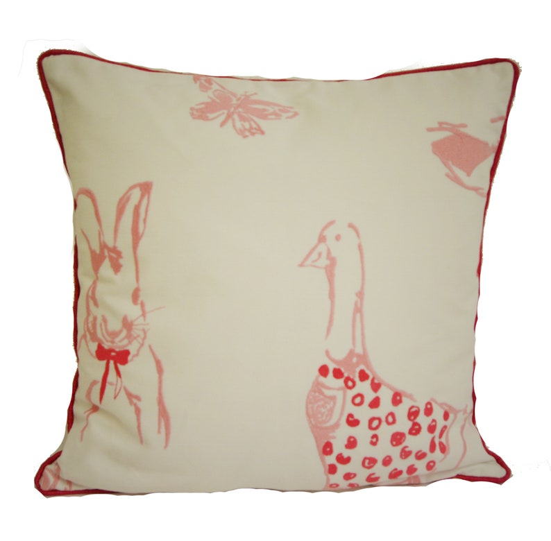 May include: A white pillow with a pink and red design featuring a rabbit and a goose. The rabbit is wearing a red bow tie and the goose is wearing a red polka dot dress.