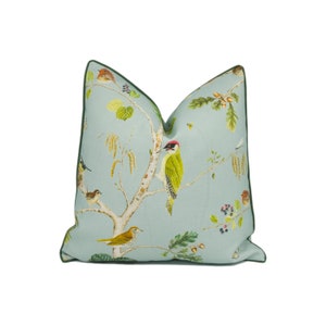 May include: A light blue cushion with a green border features a whimsical pattern of birds and branches on a light blue background.