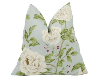 May include: A decorative throw pillow with a light blue background and a floral pattern. The pattern features large white peony flowers, green leaves, and small red berries. The pillow is a square shape.