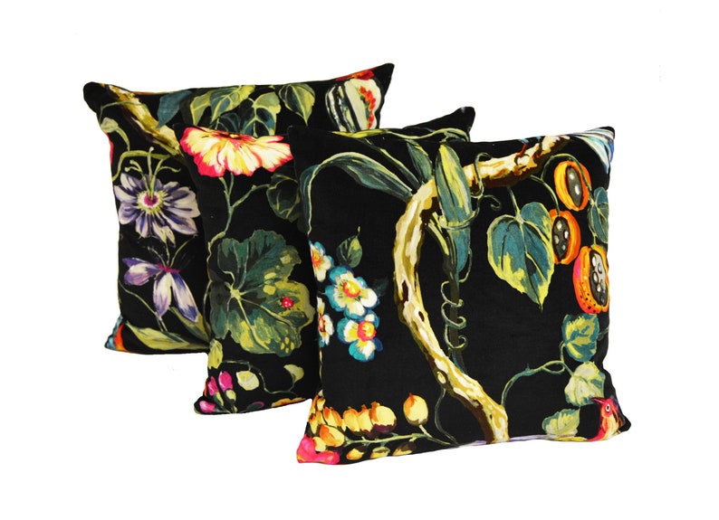 May include: Three black velvet throw pillows with a floral and fruit print. The print features bright colors like red, yellow, orange, pink, and blue.