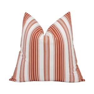 Puede incluir: Una almohada de tiro de rayas blancas y óxido con un diseño simple y moderno.