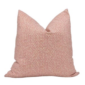 May include: A square throw pillow featuring a repeating geometric pattern of small, interlocking arrow-like shapes in a muted terracotta red color against a light cream background, creating a textured appearance across the entire surface.