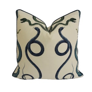 May include: A cream-colored pillow with a navy blue and green snake design. The snakes are intertwined and create a symmetrical pattern.