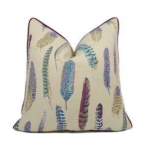 May include: A beige cushion with a burgundy trim features a colourful feather pattern. The feathers are in shades of blue, green, purple, and brown.