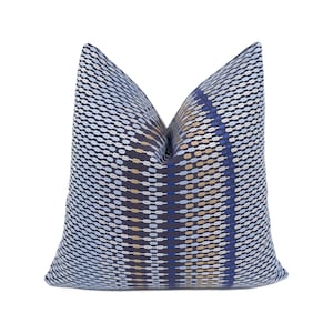 Può includere: Un cuscino decorativo con un motivo geometrico in tonalità di blu, bianco e oro. Il motivo è composto da piccole forme ovali disposte in un motivo ripetitivo.