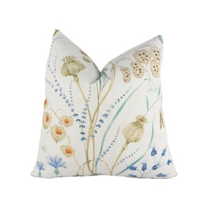 May include: A white throw pillow with a floral pattern featuring blue, green, and brown wildflowers. The pillow is made of a soft, linen-like fabric.