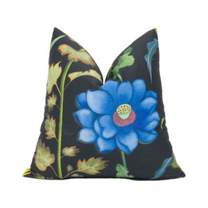May include: A black pillow with a blue flower and green leaves printed on it. The flower has a red center and yellow accents.