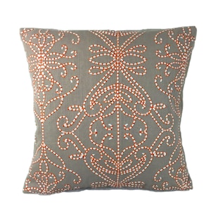 Könnte beinhalten: Grauer Dekokissen mit einem weißen und orangefarbenen gestickten Blumenmuster.