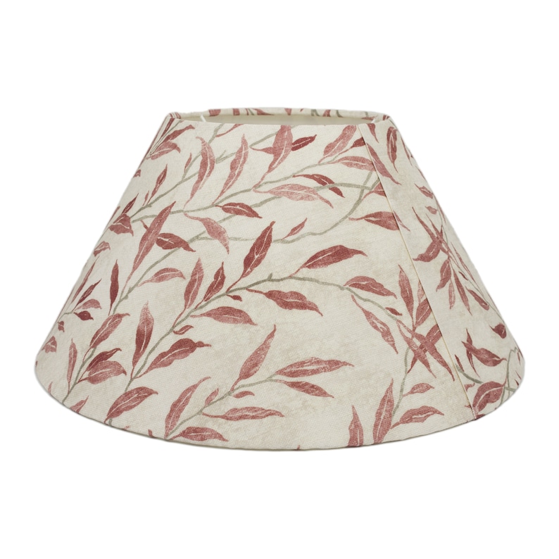May include: A cream-colored lampshade with a red leaf pattern. The shade is a cone shape and has a scalloped edge.