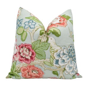 May include: Decorative throw pillow with a floral pattern. The pillow features a light blue background with large pink, red, and blue flowers, green leaves, and a bird design. The pillow is a square shape.