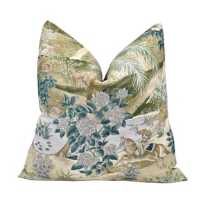 May include: Decorative throw pillow with a detailed landscape design. The pillow features a scene with deer, riders on horseback, and lush foliage in shades of green, blue, and beige. The pillow is a square shape.