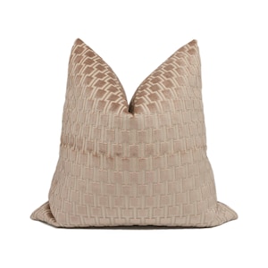 Puede incluir: Una almohada de terciopelo beige con un patrón geométrico. La almohada es cuadrada y tiene un brillo sutil.