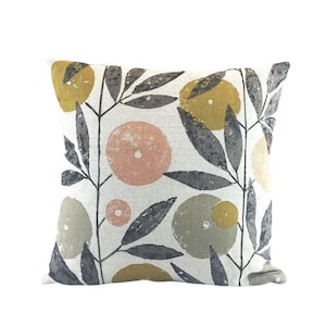 May include: A square throw pillow with a beige linen fabric background. The pillow features a repeating pattern of stylized leaves in shades of gray and brown, and circles in shades of peach, yellow, and green.