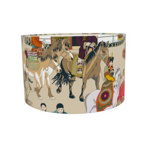 May include: A beige lampshade featuring a colourful pattern of horses and people. The design includes a horse with a rider, a horse with a saddle, and a horse with a rider holding reins. The pattern also includes people in traditional clothing.