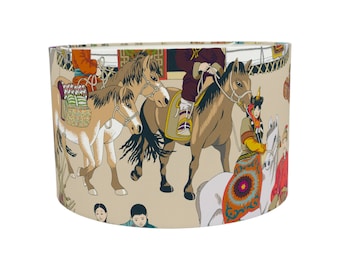 May include: A beige lampshade with a colorful pattern of horses and people. The pattern includes a horse with a rider, a horse with a saddle, and a horse with a rider holding a reins. The pattern also includes people in traditional clothing.