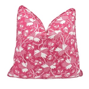 Puede incluir: Una almohada rosa con un patrón floral blanco. La almohada tiene forma cuadrada y una textura suave y mullida.