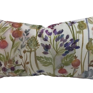 May include: A rectangular throw pillow with a white background and a watercolor floral pattern in shades of pink, purple, green, and brown. The pillow features a variety of flowers, leaves, and stems.
