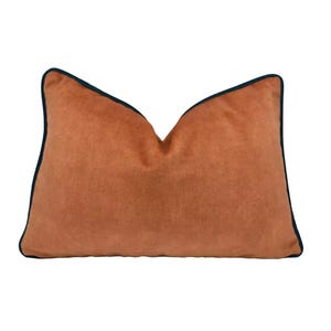 May include: A rectangular, terracotta-coloured cushion with a dark blue trim. The cushion has a soft, textured appearance and a classic shape. This decorative cushion is suitable for a bed or sofa.