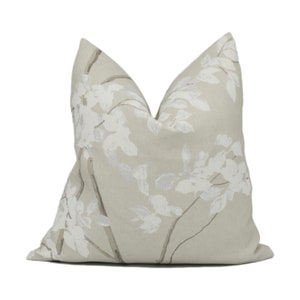 May include: A beige pillow with a white floral pattern. The flowers are stylized and resemble branches with white blossoms.