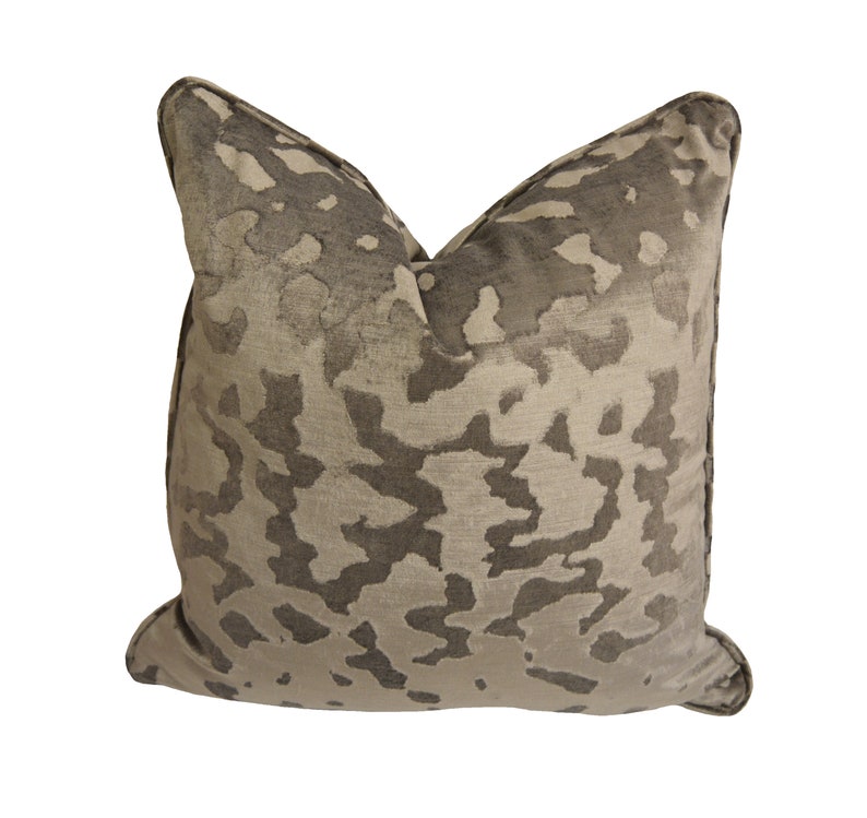 May include: A decorative cushion with a beige and brown abstract pattern. The cushion has a soft, velvety texture.