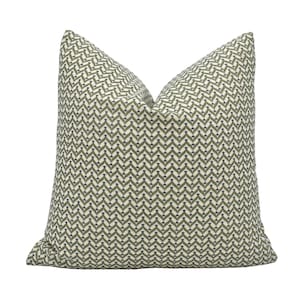 May include: Square cushion featuring a repeating geometric pattern in olive green and cream. The cushion has a soft, textured appearance and is designed for home decor.