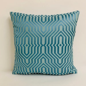 May include: A teal blue throw pillow with a geometric pattern. The pattern is made up of repeating lines and shapes that create a modern and stylish look.