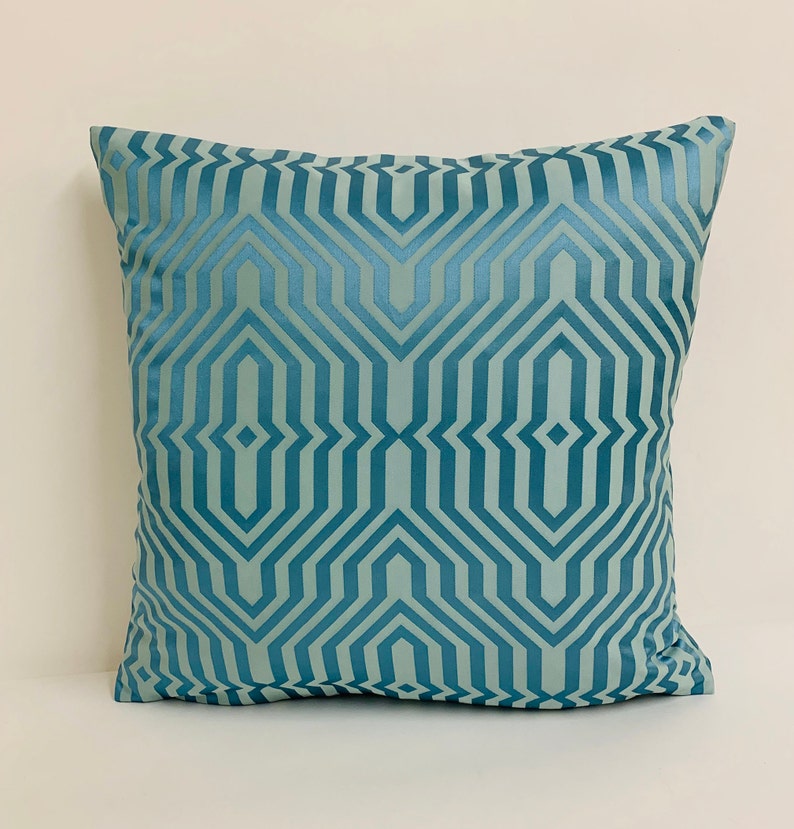 May include: A teal blue throw pillow with a geometric pattern. The pattern is made up of repeating lines and shapes that create a modern and stylish look.