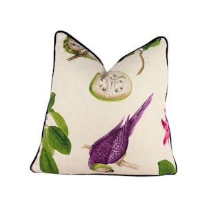 May include: A decorative throw pillow with a white background and a purple bird, green leaves, and a green fruit design.