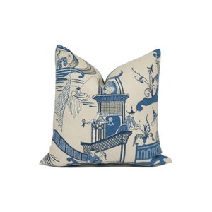 May include: A cream-coloured pillow with a blue and white Chinese-inspired design. The pillow features a pagoda, figures, and floral motifs.