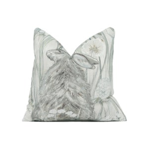 May include: A gray and white throw pillow with a watercolor illustration of a rabbit in a field of tall grass and dandelions.