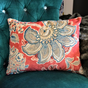 May include: A red cushion with a floral pattern in shades of blue, beige, and white. The cushion is on a green velvet chair.