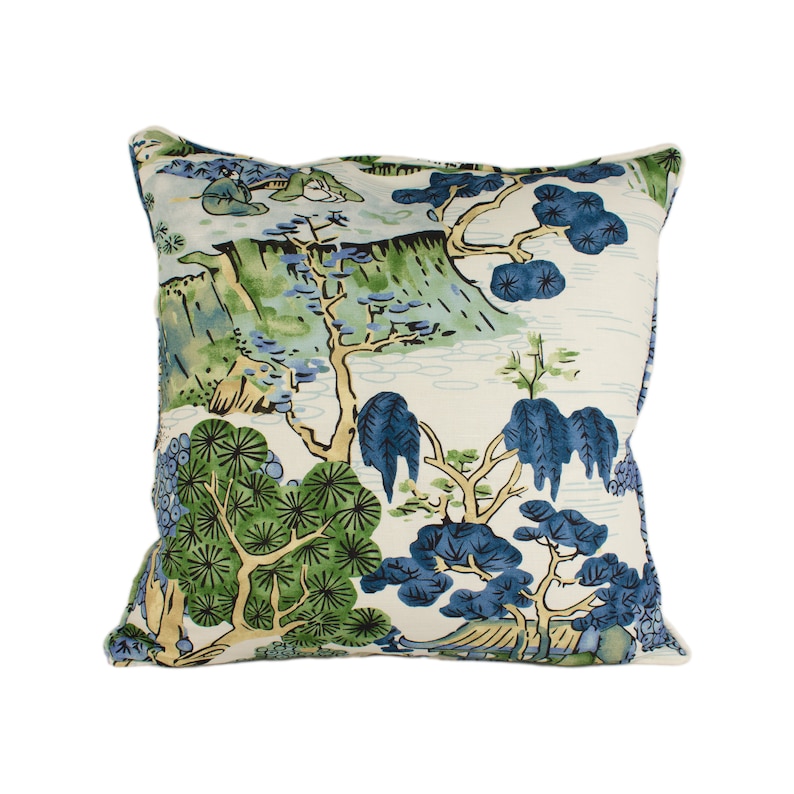 May include: A white throw pillow with a blue and green landscape design. The design features trees, mountains, and water.
