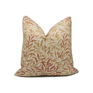 Puede incluir: Una almohada de color crema con un patrón floral marrón y naranja. El patrón presenta hojas y ramas estilizadas.