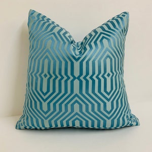 May include: A teal blue throw pillow with a geometric pattern. The pattern is made up of repeating lines and shapes that create a modern and stylish look.