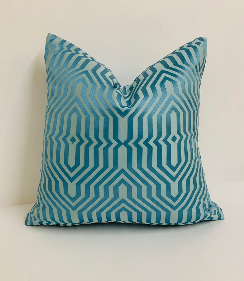 May include: A teal blue throw pillow with a geometric pattern. The pattern is made up of repeating lines and shapes that create a modern and stylish look.