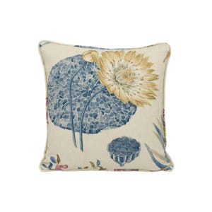 May include: A cream-coloured throw pillow with a blue and yellow floral pattern featuring lotus flowers and leaves. The pillow has a subtle texture and a light brown border.