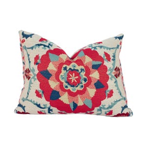 May include: Decorative throw pillow with a floral design. The pillow features a large, central red flower with blue and cream accents. The background is cream-colored with blue floral patterns.