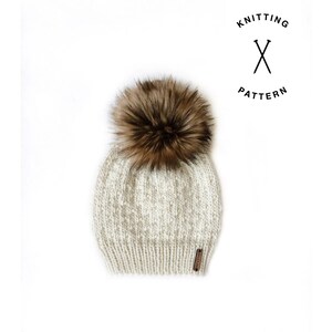 May include: A white and beige knitted beanie with a brown faux fur pom pom. The beanie has a small brown leather tag with the word "KNITTING" on it.