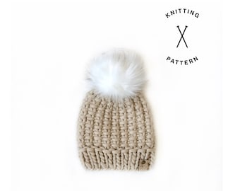 May include: A beige knitted beanie with a white pom pom. The beanie has a small brown leather tag with the text "Knitting Pattern" on it.
