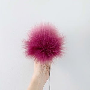 May include: A large, fluffy pink pom pom with a black string attached.