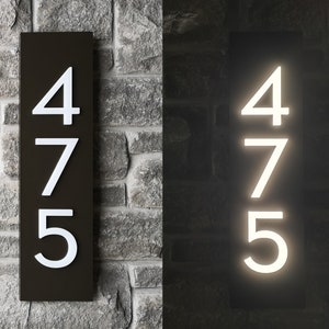 May include: A black house number plaque with white numbers 475. The plaque is illuminated in the second image.