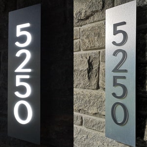 May include: A silver metal house number sign with the number 525 displayed in black. The sign is mounted on a brick wall.