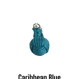 May include: A small, round, Caribbean blue knot charm with a silver-colored metal loop at the top. The text "Caribbean Blue" is displayed in a bold, black font below the charm.