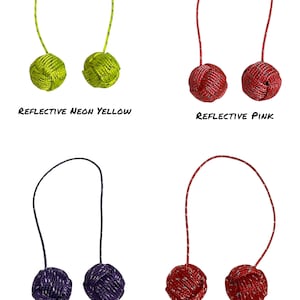 May include: Four pairs of decorative knot balls in neon yellow, pink, purple, and red. Each pair has a loop and is labelled with the colour and the word "reflective". The neon yellow pair has a green loop, the pink pair has a red loop, the purple pair has a dark blue loop, and the red pair has a red loop.