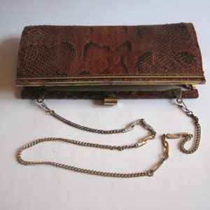 Könnte beinhalten: Eine braune Clutch aus Schlangenleder mit einer goldenen Kettenkette. Die Clutch hat einen Verschluss aus Metall.