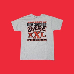 May include: Gray t-shirt with the text "PROPERTY OF BROWN COUNTY SHERIFF D.A.R.E. XXL PROGRAM" in black and red lettering.