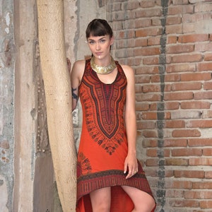 Può includere: Abito arancione con collo all'americana e motivo geometrico nero, con orlo asimmetrico. L'abito senza maniche presenta un motivo decorativo sul corpetto. La modella indossa sandali neri con dettagli dorati. Il logo del marchio è visibile.