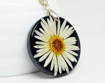 May include: A silver chain necklace with a circular pendant. The pendant showcases a white daisy flower with a yellow centre set against a black backdrop. The pendant is approximately 3.8 cm in diameter.