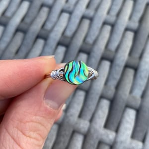 May include: A silver wire wrapped ring with a green, blue, and iridescent abalone shell inlay.
