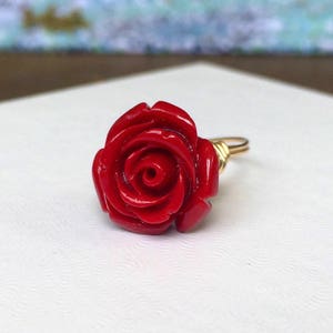 May include: A red rose ring made of coral with a gold wire wrapping.